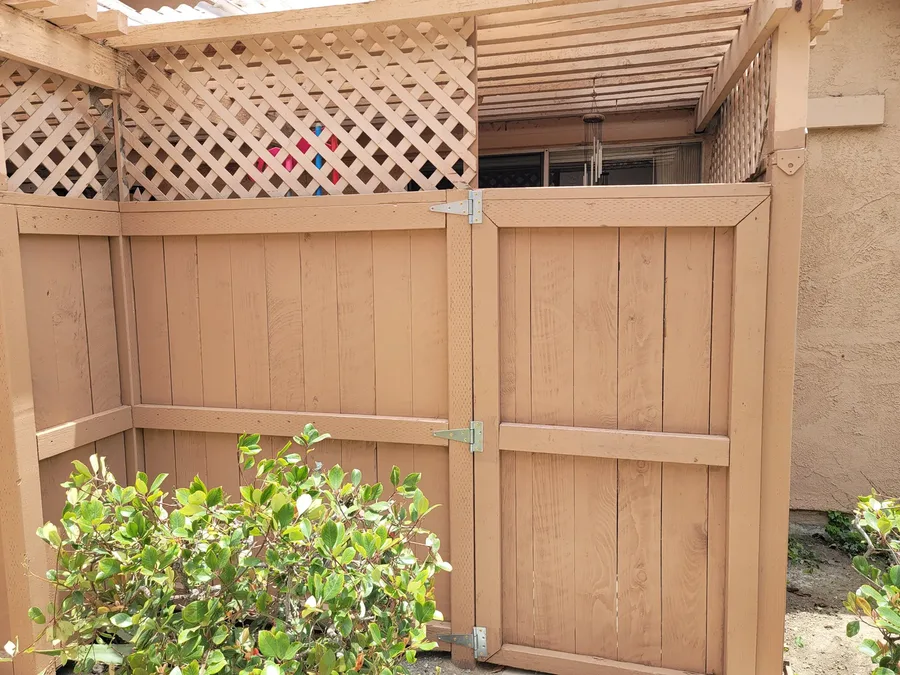 Freshly stained wood fence and matching gate with new galvanized hinges and a lattice screen along the top