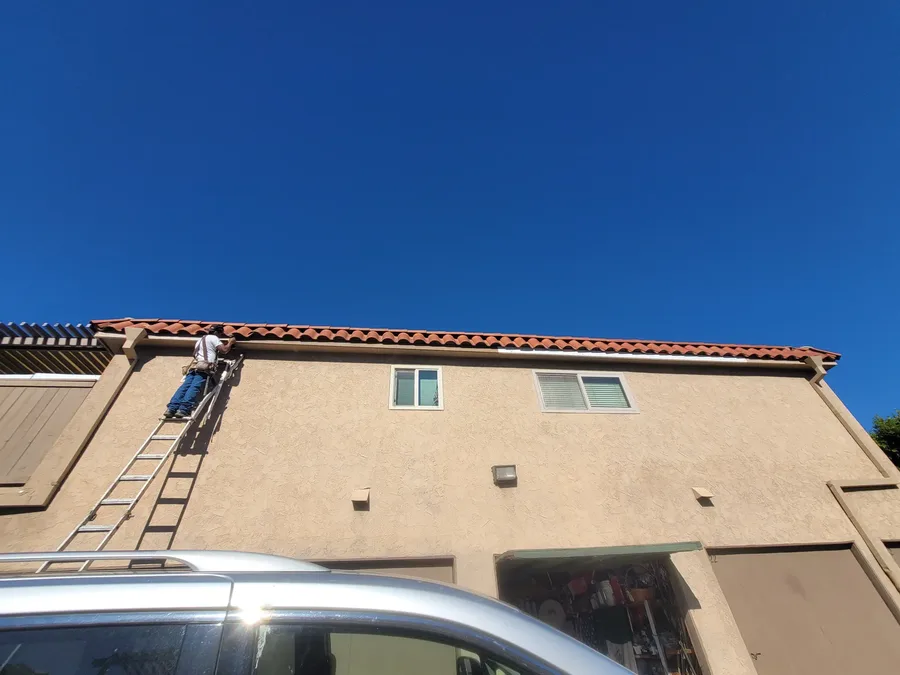 Extension ladder set against a two story stucco building with a tile roof, one of the crew working on the fascia at the roof line